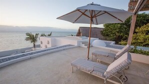 A sunlit outdoor lounge area with a large umbrella, lounge chairs, and a view of the sea. - Bahia Mar Beach House (Vilanculos)
