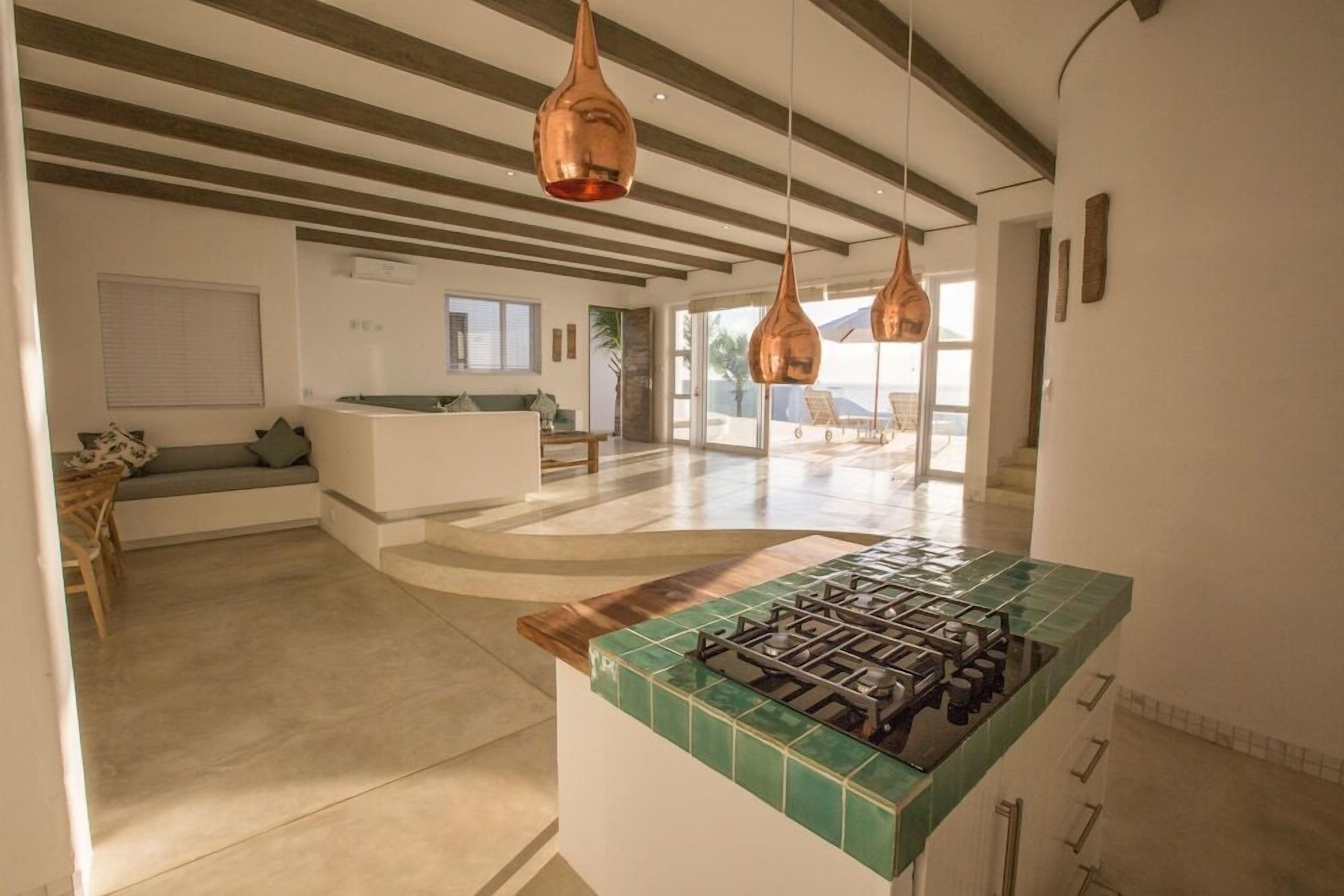 A modern kitchen with a gas stove, a green-tiled countertop, and hanging copper pendant lights.