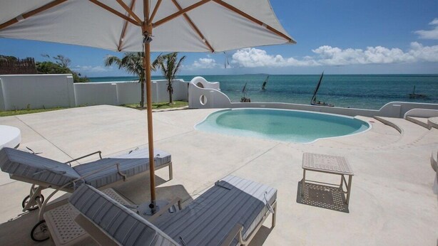 A poolside area with lounge chairs, a table, and an umbrella. - Bahia Mar Beach House (Vilanculos)