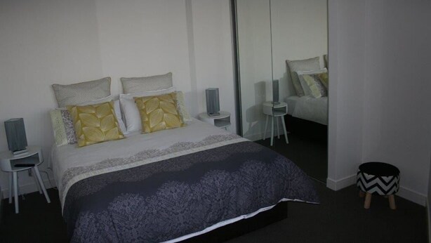 A modern bedroom with a large bed, bedside tables, a mirror, and a small stool.