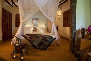 Cama com dossel e cortina decorativa, mesa de cabeceira com garrafa e copos, e arandelas fixadas na parede.