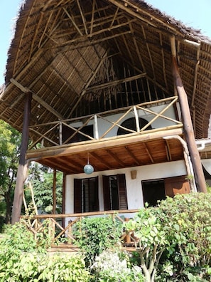 Een traditionele structuur met rieten dak en houten balkon, omringd door groen.
