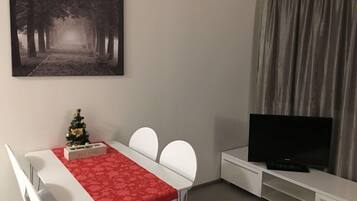 A modern living room with a dining area, a flat-screen TV, and a Christmas tree.