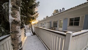 A snow-covered wooden deck with a railing, leading to a building with multiple windows and a door. - Arctic Resort Delight (Rovaniemi)