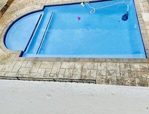 A rectangular swimming pool with a curved section on one side, surrounded by stone tiles. - Airport Diamond Guest House (Kempton Park)