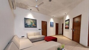 Amplia sala de estar con un sofá color crema, un reposapiés rojo y dos plantas en macetas.