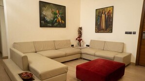 Una sala de estar con un sofá seccional color beige, un reposapiés rojo y dos cuadros en la pared.