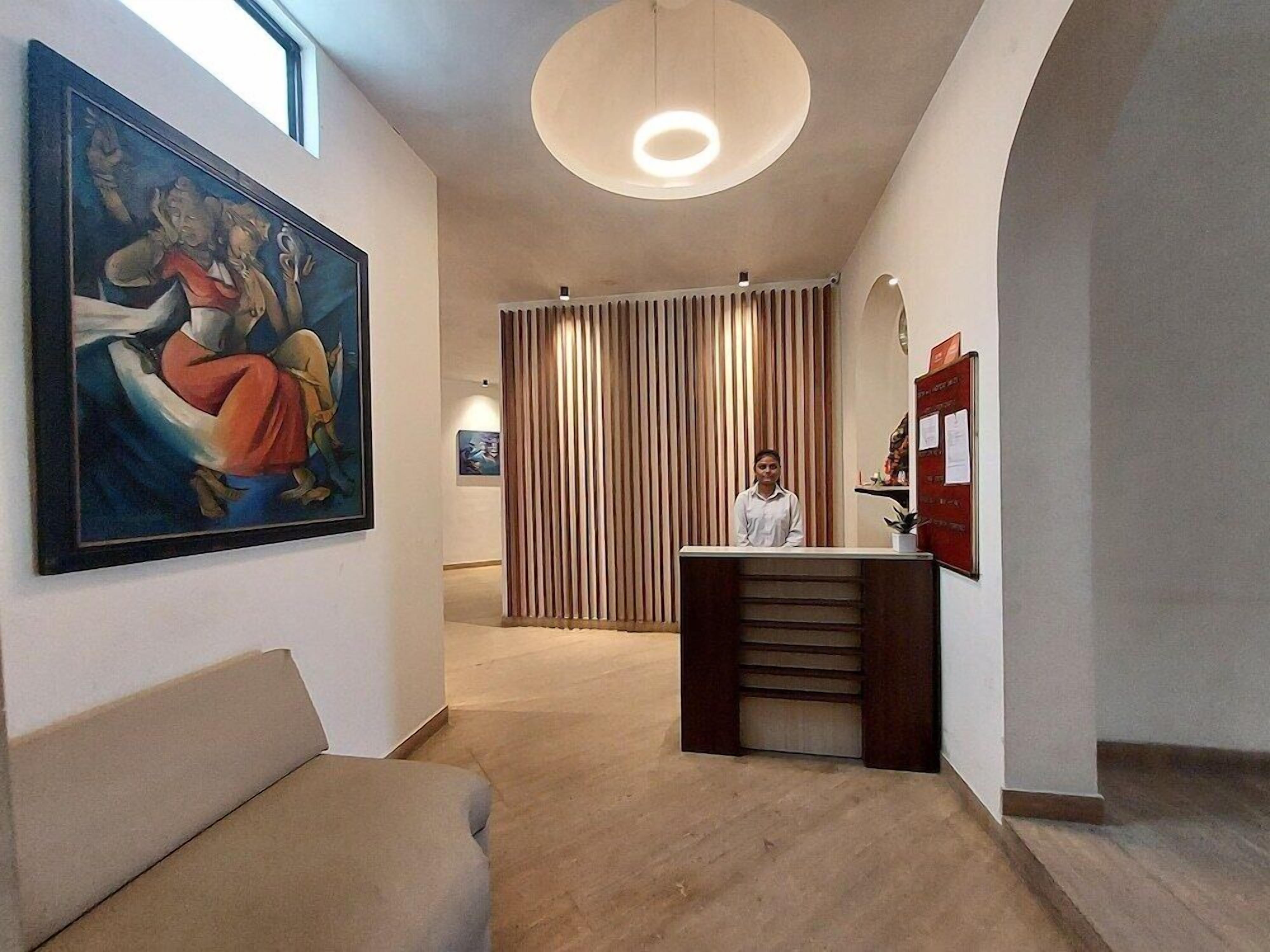 A hotel lobby with a reception desk, a large painting on the wall, and a modern ceiling light.