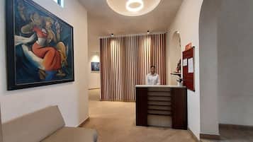 A hotel lobby with a reception desk, a large painting on the wall, and a modern ceiling light.