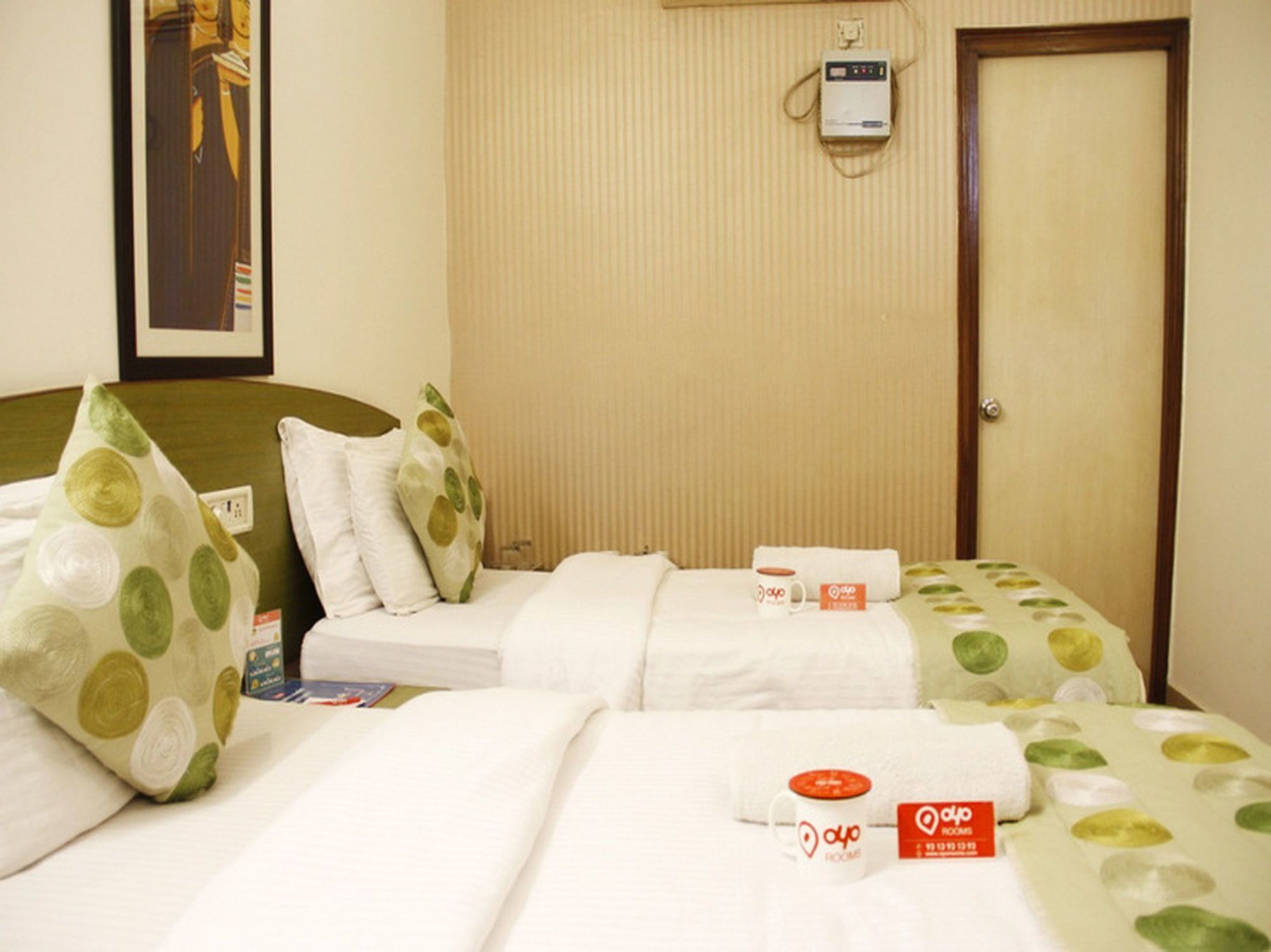A hotel room with two beds, a wall-mounted heater, and a door.