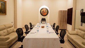 Un salón de conferencias con una larga mesa, sillas, botellas de agua, una computadora portátil y un cuadro en la pared.