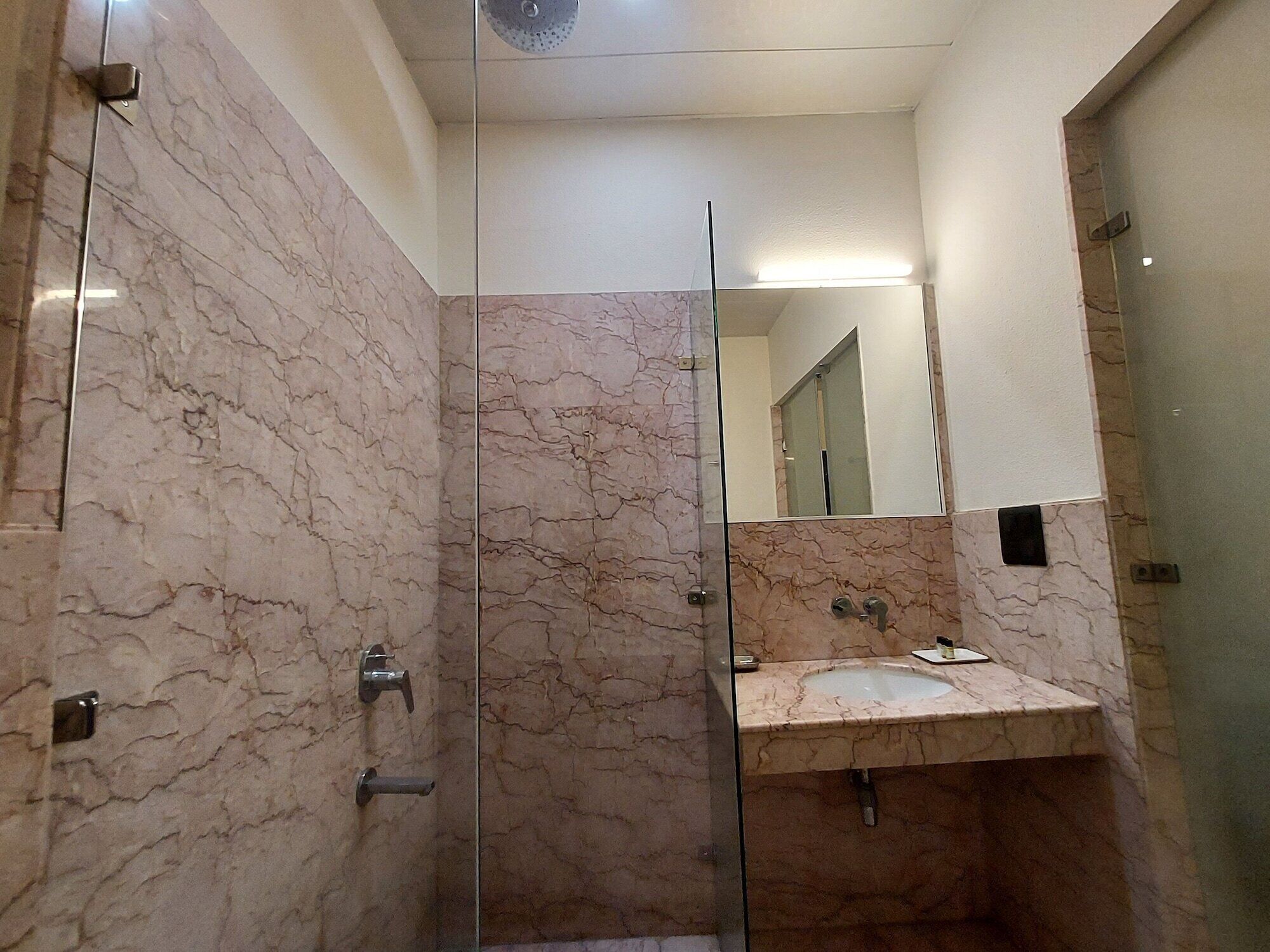 A modern bathroom with marble walls, a glass shower enclosure, and a sink with a mirror above it.