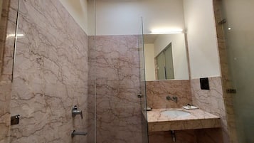 A modern bathroom with marble walls, a glass shower enclosure, and a sink with a mirror above it.