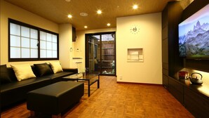 A modern living room with a sofa, ottoman, and a television displaying a mountainous landscape. - Machiya Kaemon Kyoto sta (Kyoto)
