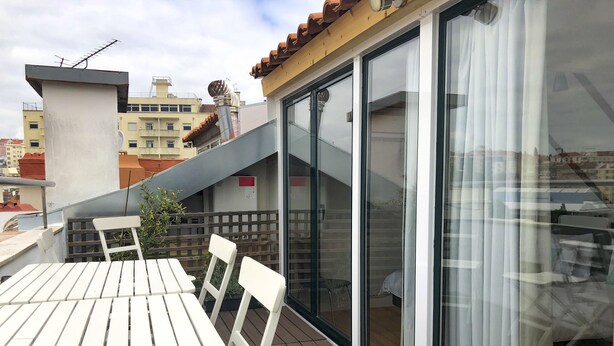 Un balcón con mesa y sillas, un ventanal corredero y vistas de la ciudad.