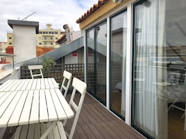Un balcón con mesa y sillas, un ventanal corredero y vistas de la ciudad.