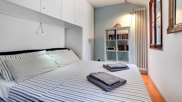 Un dormitorio con cama, estantería y radiador.