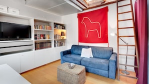 Una sala de estar moderna con un sofá azul, un televisor de pantalla plana, estanterías y una silueta de un caballo rojo en la pared.