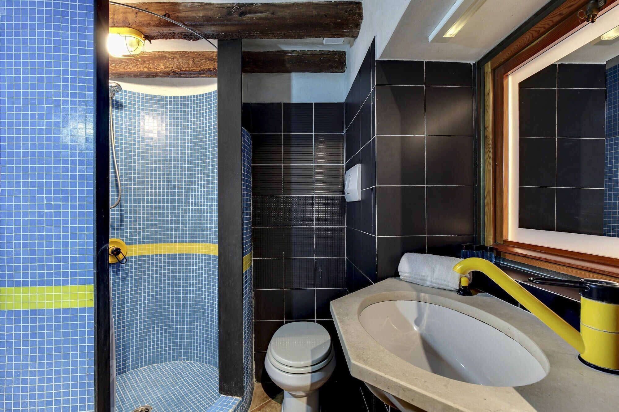 A bathroom with a blue-tiled shower, a toilet, and a sink with a yellow faucet.
