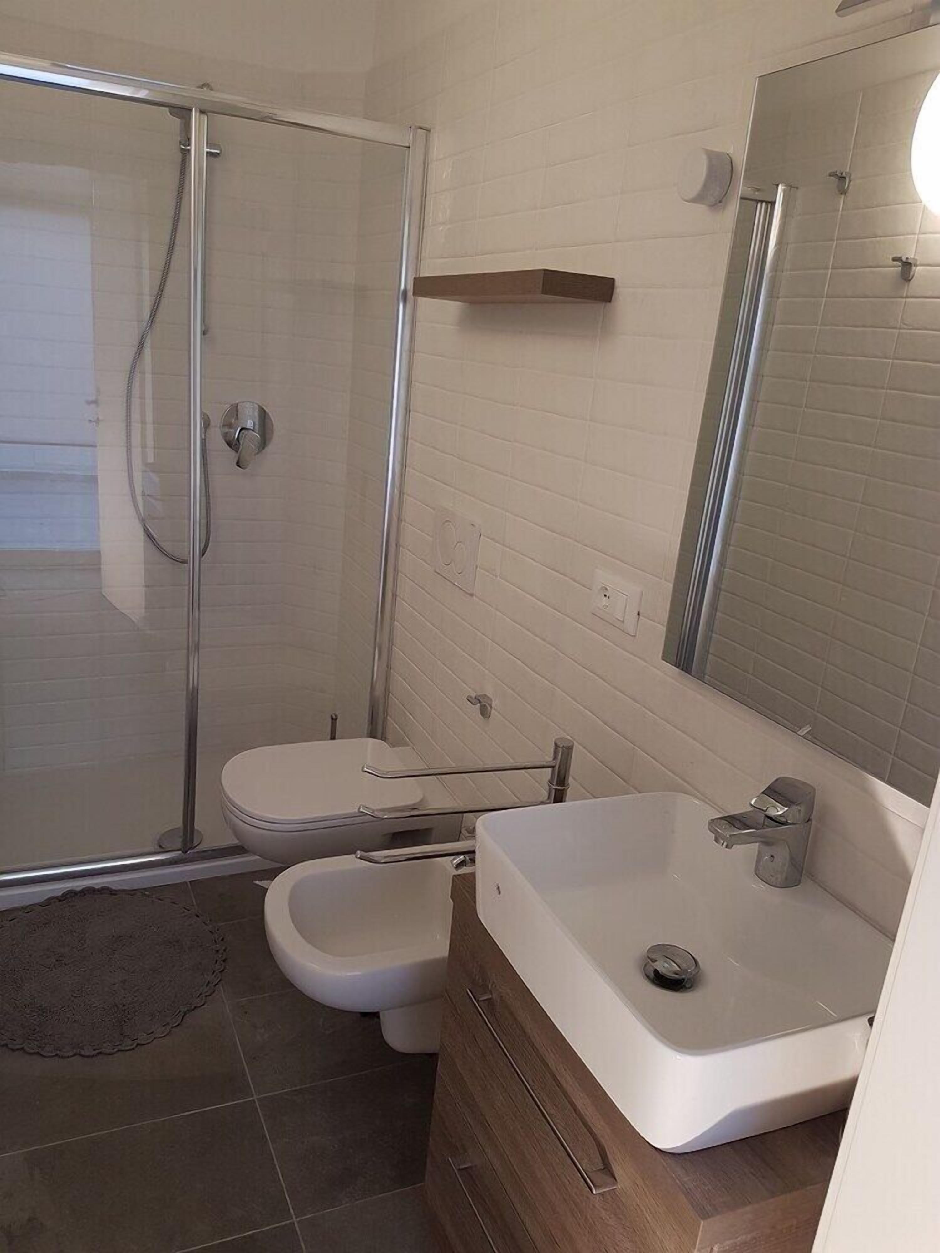 A modern bathroom with a glass shower enclosure, a white toilet, a bidet, and a sink with a mirror.