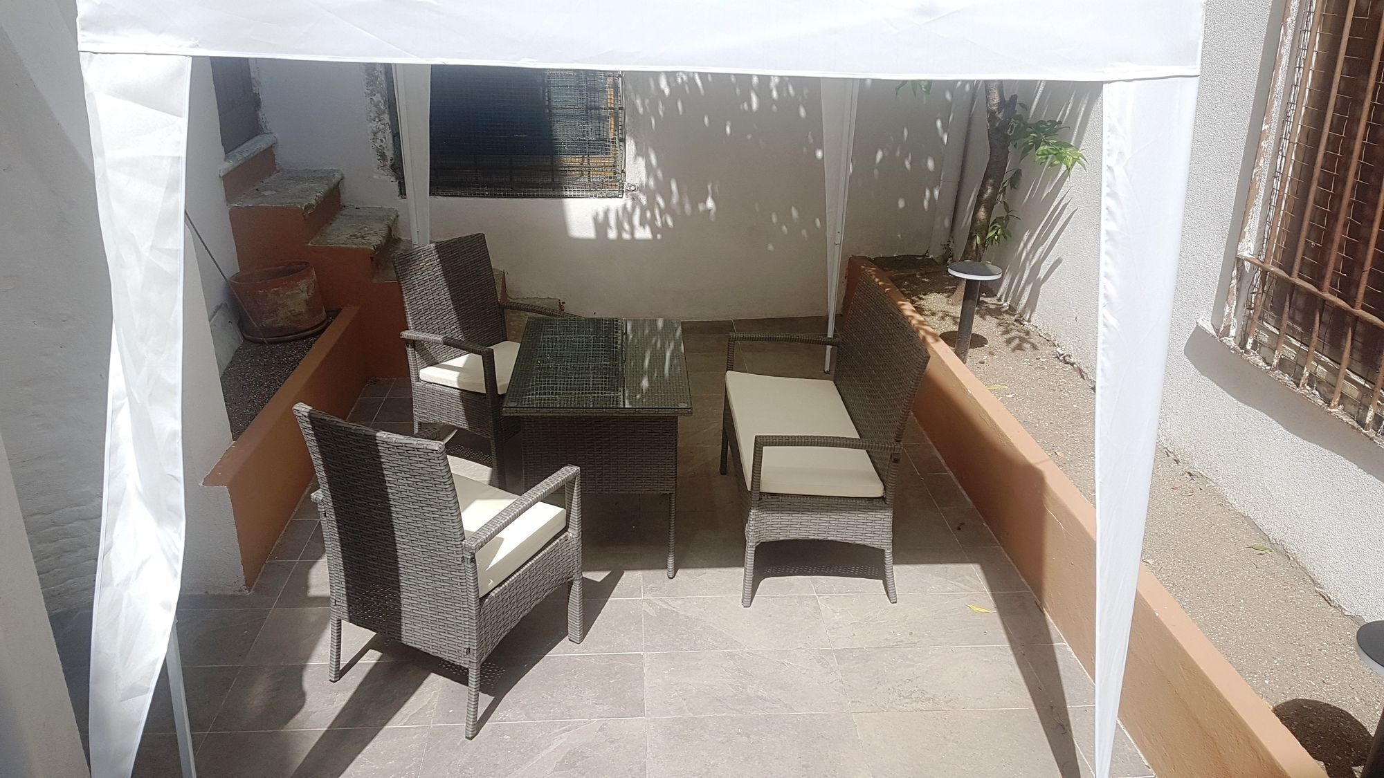 Eine Terrasse mit Korbmöbeln, einem Glastisch und einem weißen Baldachin.