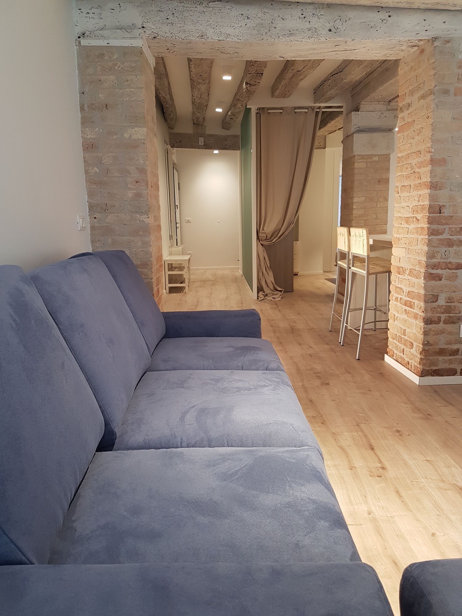 Un salon moderne avec des murs en briques apparentes, un plancher en bois et un canapé d’angle gris.