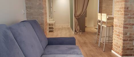 Un salon moderne avec des murs en briques apparentes, un plancher en bois et un canapé d’angle gris.