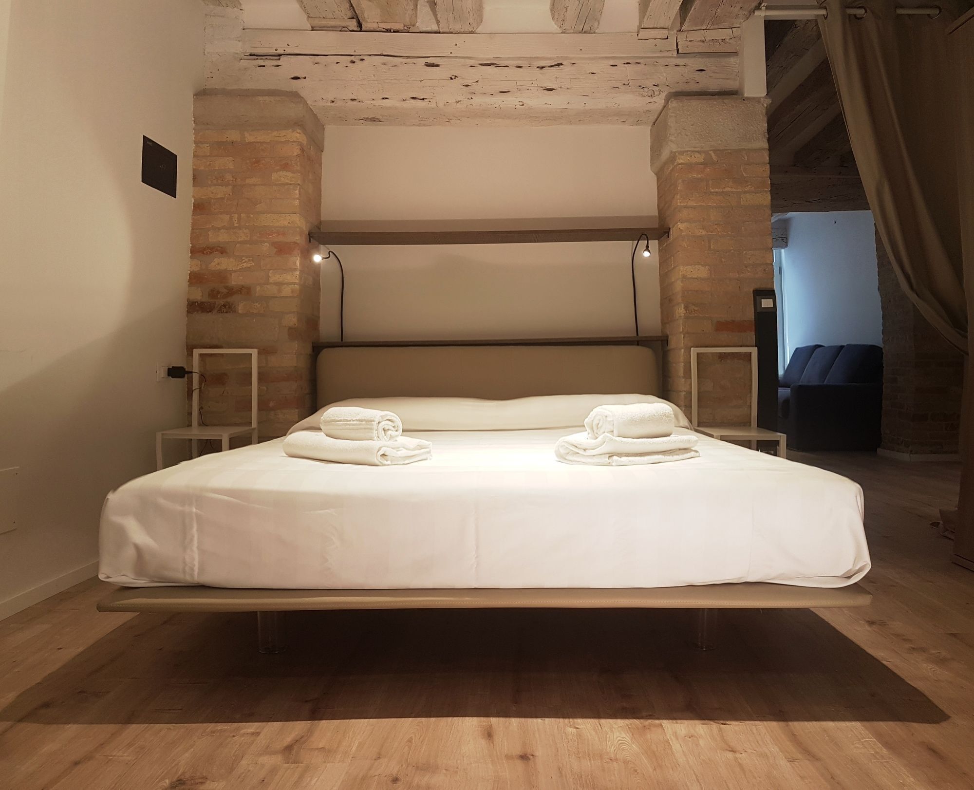 A bed with a headboard, two bedside tables, and two rolled towels on the bed.