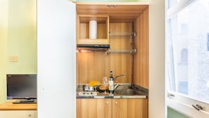 A compact kitchen with wooden cabinets, a built-in stove, and a window overlooking a building.