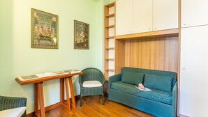 A compact room with a green sofa, a wicker chair, a wooden table, and two framed pictures on the wall.
