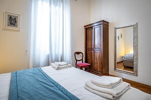 Um quarto com uma cama, guarda-roupa de madeira, uma cadeira, um espelho e um quadro na parede.