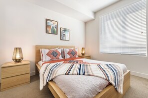 Ein ordentlich eingerichtetes Schlafzimmer mit einem Bett, zwei Nachttischen und einem Fenster mit Jalousien.