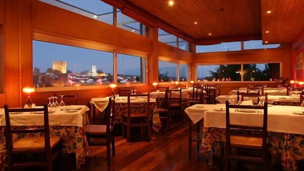Un restaurant doté de nombreuses tables et chaises, avec de grandes fenêtres offrant une vue sur le paysage urbain au crépuscule.