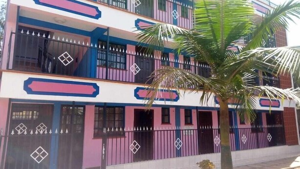 Edifici de diversos pisos amb balcons, una palmera al primer terme i una entrada tancada amb reixa.