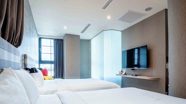 A hotel room with two beds, a TV, a desk, and a window. - Double Pretty Hotel (Taichung)