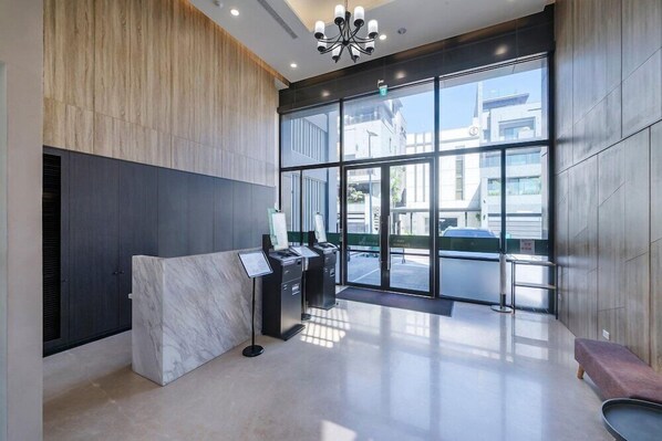 A modern reception area with a marble counter, glass doors, and a view of the street outside. - H Inn (Taichung)