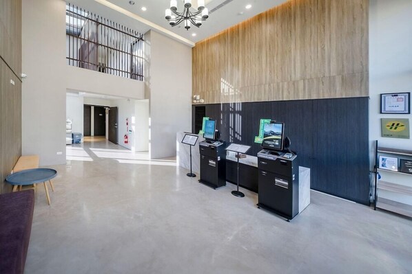 A modern reception area with a high ceiling, a mezzanine level, and a reception desk with digital kiosks. - H Inn (Taichung)