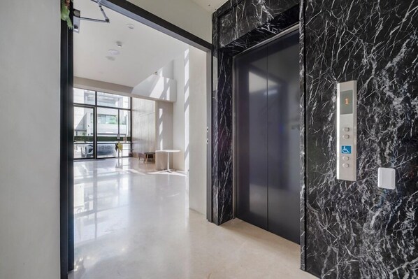 A modern elevator with marble walls and a control panel with accessibility features. - H Inn (Taichung)