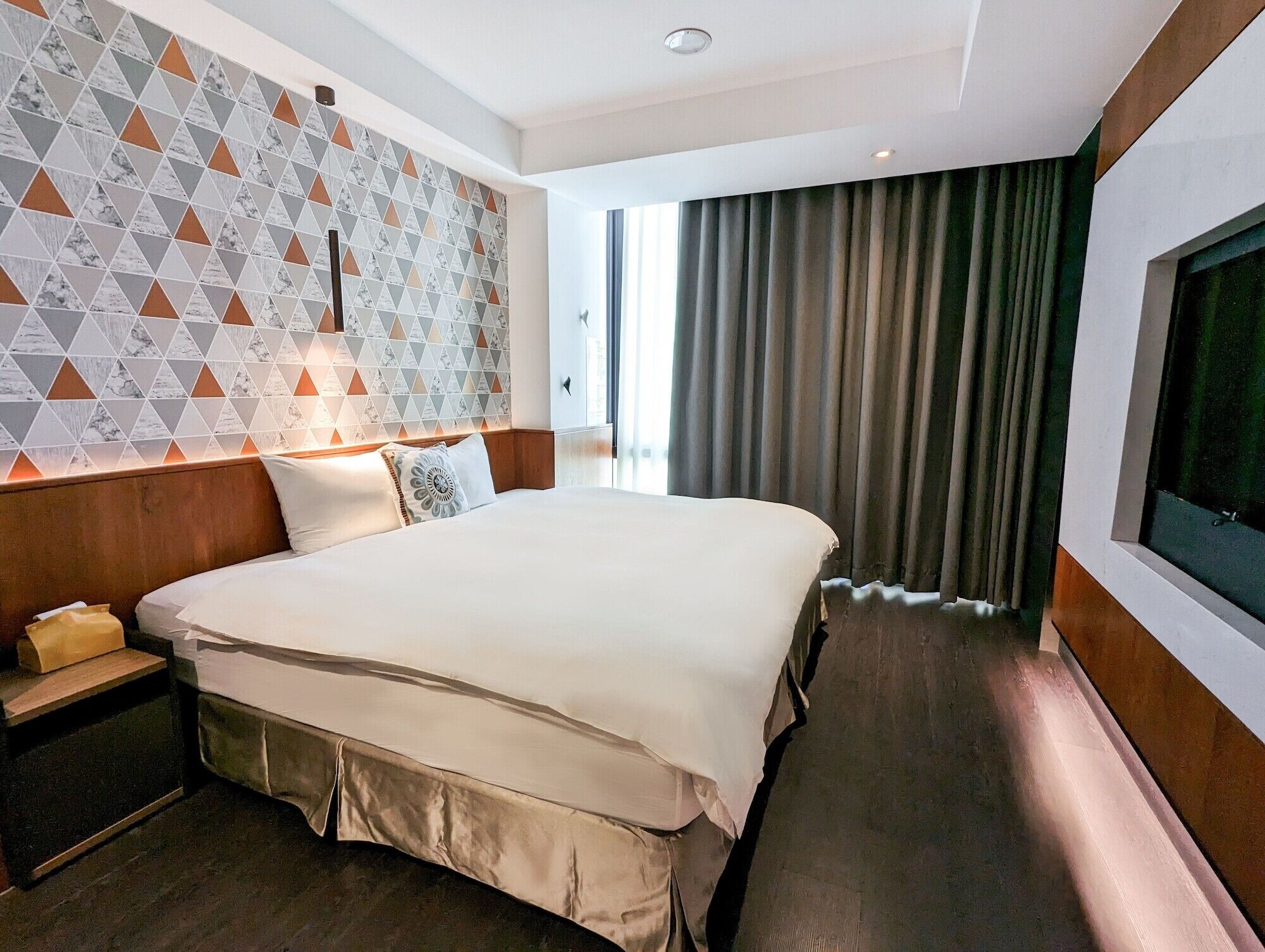 A hotel room with a large bed, a nightstand, a TV, and a patterned wall.