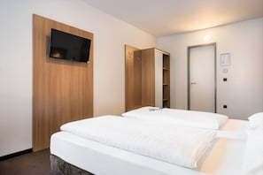 A hotel room with a bed, a TV mounted on a wooden panel, a wardrobe, and a door with a light. - Garner Hotel Stuttgart - Zuffenhausen By IHG (Stuttgart)