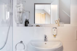 Une salle de bain moderne avec une douche à parois de verre, un lavabo blanc, un miroir et des articles de toilette disposés sur le comptoir.
