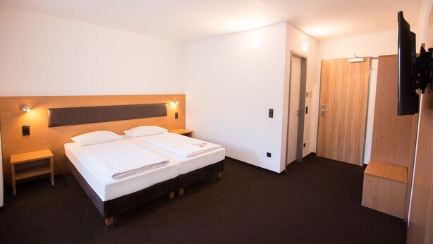 A hotel room with a double bed, bedside tables, a wooden headboard, a wardrobe, and a television. - Garner Hotel Stuttgart - Zuffenhausen By IHG (Stuttgart)