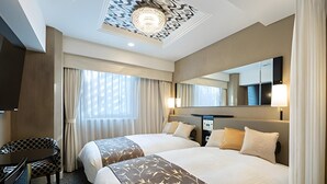 Een hotelkamer met twee bedden, een bureau, een stoel, een grote spiegel en een plafondlamp.