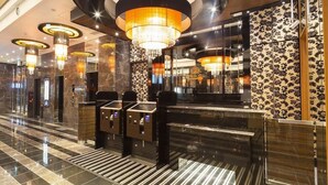 Een moderne hotel lobby met een marmeren vloer, een centraal hanglamp en een receptiebalie.