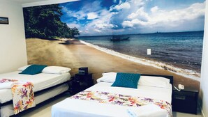 Ein Zimmer mit zwei Betten, jedes mit einer weißen Matratze und einer farbenfrohen Blumenbettdecke. An der Wand hinter den Betten ist ein Wandbild mit einer Strandansicht zu sehen.