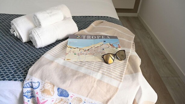 A neatly made bed with folded white towels, a striped blanket with sea-themed prints, a map, and a pair of sunglasses. - La Torre del Mulino Accomodation (Tropea)
