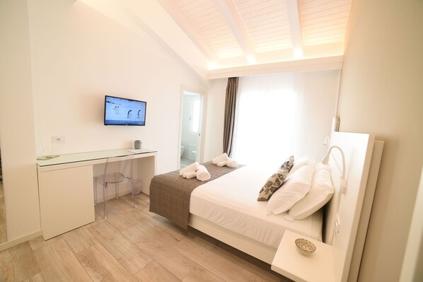 A bedroom with a bed, a desk, a television, and a window with curtains.