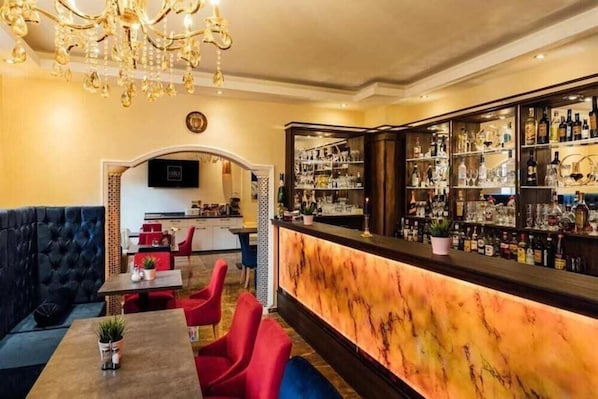 A bar area with a marble countertop, red chairs, and a chandelier. - Hotel Austria (Hamburg)
