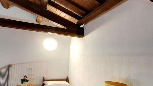 A bedroom with a wooden ceiling, a single bed, a bedside table with a lamp, and a radiator. - Hostel Marina (Cagliari)