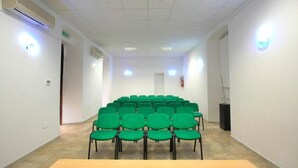 A conference room with rows of green chairs, a wooden table, white walls, and ceiling lights. - Hostel Marina (Cagliari)